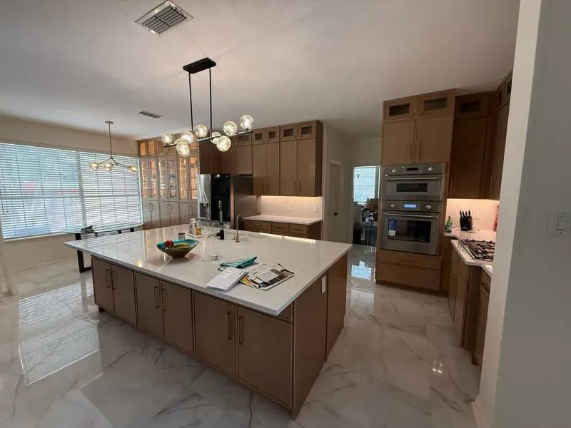 Open kitchen with wood flat-panel cabinets, built-in double ovens and a large white quartz island, by Acue Marmonite