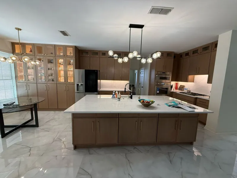 Kitchen with wood-tone flat-panel cabinets, lit glass uppers and a large white quartz island, by Acue Marmonite