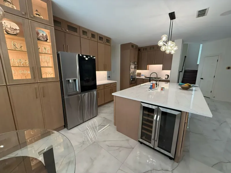 Kitchen with glass-front wood cabinets and a white quartz island with wine fridge, by Acue Marmonite